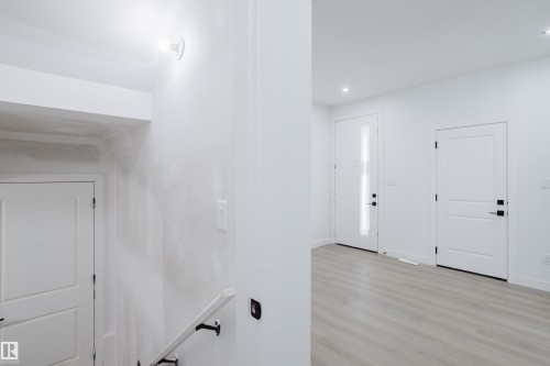 Bright entryway featuring a modern white door with a vertical frosted glass panel, contemporary black hardware, and light wood-finish flooring - 8728 182 Avenue Nw, Edmonton, AB - Indoor Photo Showing Other Room
