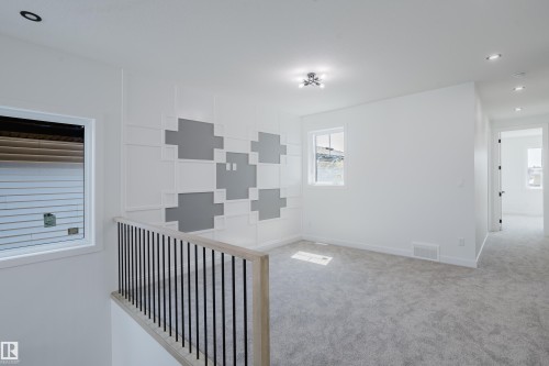 Carpeted loft area featuring a decorative accent wall with geometric paneling, a modern black metal and wood-finish railing, recessed lighting, and a contemporary ceiling fixture - 8728 182 Avenue Nw, Edmonton, AB - Indoor Photo Showing Other Room