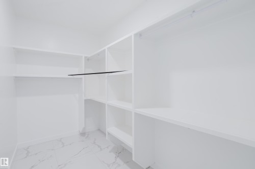 Spacious closet featuring white built-in shelving, hanging rods, and light-toned marble-look tile flooring - 8728 182 Avenue Nw, Edmonton, AB - Indoor