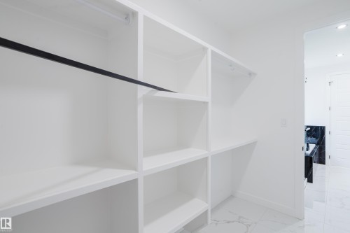 Built-in white shelving system featuring multiple compartments and a black hanging rod - 8728 182 Avenue Nw, Edmonton, AB - Indoor Photo Showing Other Room