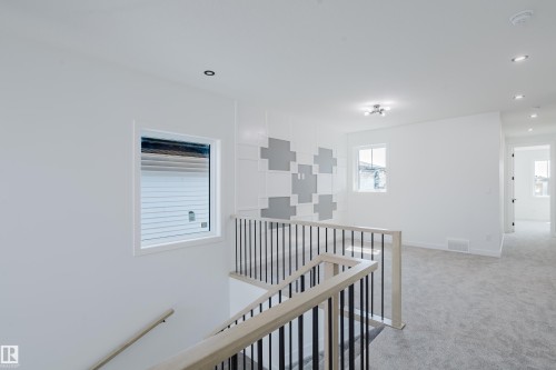 Upper-level landing with light-toned carpet flooring, a modern black metal and light wood-finish staircase railing, and recessed ceiling lighting - 8728 182 Avenue Nw, Edmonton, AB - Indoor
