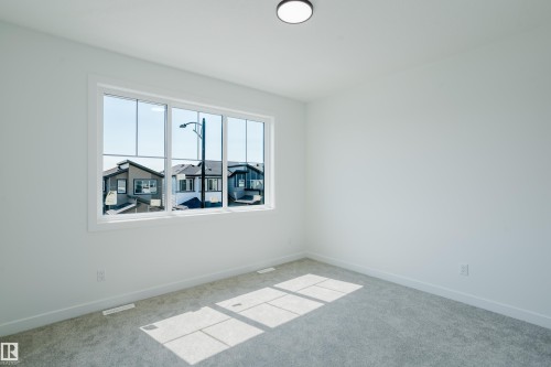 Bright room featuring a multi-pane window with white trim, light gray carpet flooring, white walls, and a contemporary flush-mount ceiling light fixture - 8728 182 Avenue Nw, Edmonton, AB - Indoor Photo Showing Other Room