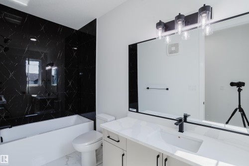 Contemporary bathroom featuring a black and white design with a white soaking tub, black tiled shower surround, and a vanity with an integrated sink and black hardware - 8728 182 Avenue Nw, Edmonton, AB - Indoor Photo Showing Bathroom