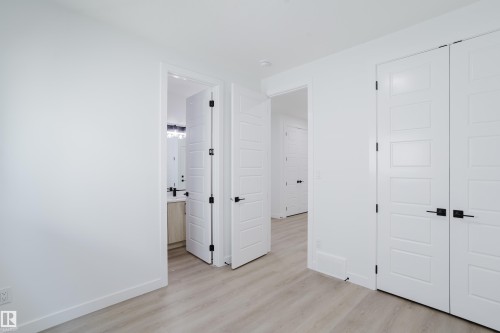 Light wood-finish flooring throughout, featuring a white paneled door with black hardware, a light wood vanity, and a modern light fixture - 8728 182 Avenue Nw, Edmonton, AB - Indoor Photo Showing Other Room