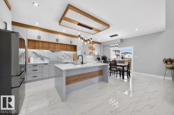 Modern kitchen featuring white high-gloss cabinetry, wood-finish accents, and a large central island with a waterfall countertop - 