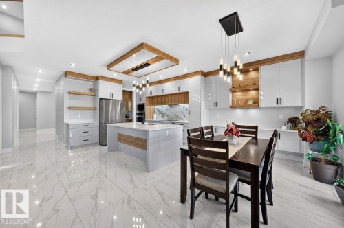 Open-concept kitchen and dining area featuring large-format tile flooring, a central island with integrated seating, stainless steel appliances, and a wood-accented ceiling feature with recessed lighting - 6001 19 Street, Nisku, AB - Indoor