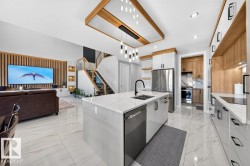Contemporary kitchen featuring a large center island with integrated sink, stainless steel appliances, and sleek white cabinetry with wood-finish accents - 