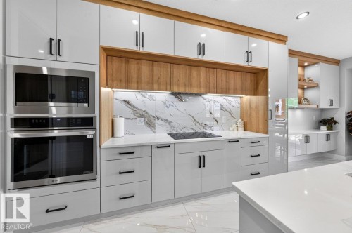 Modern kitchen featuring white high-gloss cabinetry with black hardware, integrated stainless steel appliances, a white patterned backsplash, and wood-finish accents - 6001 19 Street, Nisku, AB - Indoor Photo Showing Kitchen
