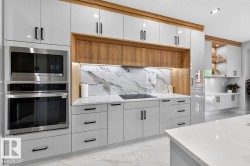 Modern kitchen featuring white high-gloss cabinetry with black hardware, integrated stainless steel appliances, a white patterned backsplash, and wood-finish accents - 