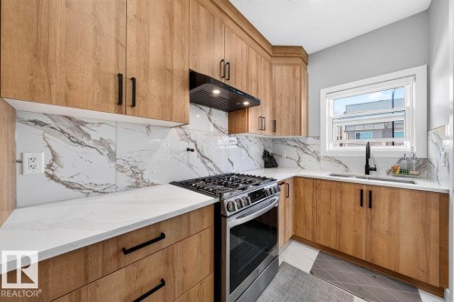 U-shaped kitchen featuring light wood-finish cabinetry with black hardware, white countertops, and a white and grey veined backsplash - 6001 19 Street, Nisku, AB - Indoor Photo Showing Kitchen