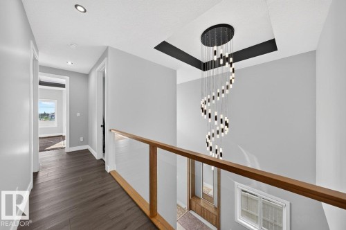 Foyer featuring a multi-tiered chandelier, recessed lighting, wood-finish flooring, and a clear panel railing with a wood-tone top rail - 6001 19 Street, Nisku, AB - Indoor Photo Showing Other Room