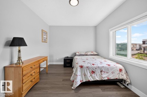 Bedroom featuring light gray walls, wood-finish flooring, a contemporary ceiling light fixture, and a large window with white trim - 6001 19 Street, Nisku, AB - Indoor Photo Showing Bedroom