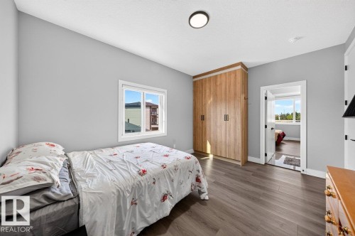 Bedroom featuring wood-finish flooring, a built-in wardrobe with wood-look doors, a white frame window, and a flush-mount ceiling light - 6001 19 Street, Nisku, AB - Indoor Photo Showing Bedroom