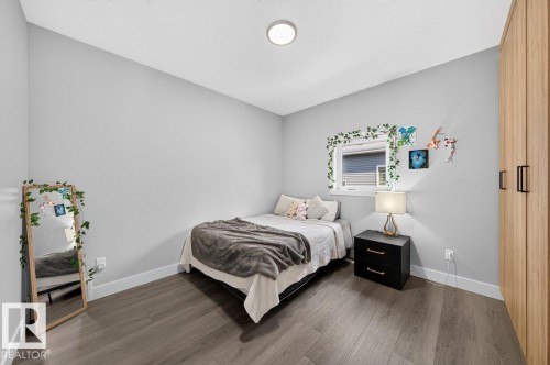 Light-filled bedroom featuring wood-finish flooring, a window with horizontal blinds, neutral wall tones, and a built-in wardrobe with black hardware - 6001 19 Street, Nisku, AB - Indoor Photo Showing Bedroom
