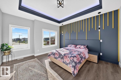Spacious room featuring wood-finish flooring, two large windows, a tray ceiling with integrated lighting, and a decorative accent wall with vertical gold elements - 6001 19 Street, Nisku, AB - Indoor Photo Showing Bedroom