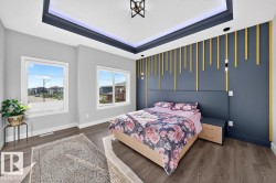 Spacious room featuring wood-finish flooring, two large windows, a tray ceiling with integrated lighting, and a decorative accent wall with vertical gold elements - 