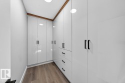Custom closet system featuring high-gloss white cabinetry, matte black hardware, integrated drawers, recessed lighting, and wood-finish flooring - 