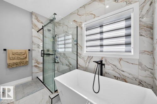 Contemporary bathroom featuring a freestanding soaking tub with a floor-mounted matte black faucet, a glass-enclosed shower with black hardware, and large format marble-look wall and floor tiles - 6001 19 Street, Nisku, AB - Indoor