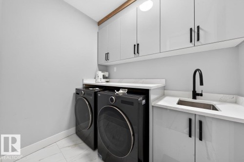 Utility area featuring light grey cabinetry with black hardware, white countertops, a stainless steel sink with a matte black faucet, and white tile flooring - 6001 19 Street, Nisku, AB - Indoor Photo Showing Laundry Room