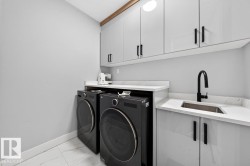Utility area featuring light grey cabinetry with black hardware, white countertops, a stainless steel sink with a matte black faucet, and white tile flooring - 