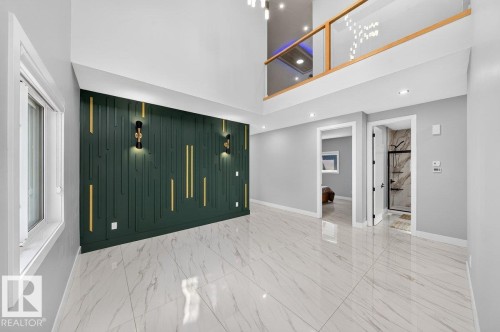 Two-story room featuring a high ceiling, a decorative accent wall with vertical paneling and sconce lighting, polished tile flooring, and an upper-level balcony with a glass and wood railing - 6001 19 Street, Nisku, AB - Indoor Photo Showing Other Room