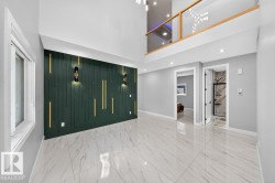 Two-story room featuring a high ceiling, a decorative accent wall with vertical paneling and sconce lighting, polished tile flooring, and an upper-level balcony with a glass and wood railing - 