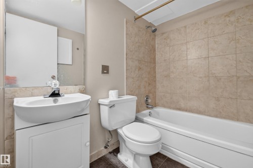 Full bathroom featuring a white porcelain tub with integrated shower, beige tiled surround, and a coordinating vanity with a white basin and mirrored medicine cabinet - #1804 10883 Saskatchewan Dr Nw, Edmonton, AB - Indoor Photo Showing Bathroom