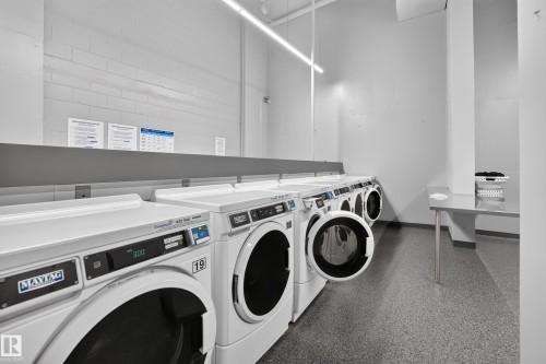 Laundry facility featuring multiple front-loading washing machines, durable flooring, and a folding counter - #1804 10883 Saskatchewan Dr Nw, Edmonton, AB - Indoor Photo Showing Laundry Room