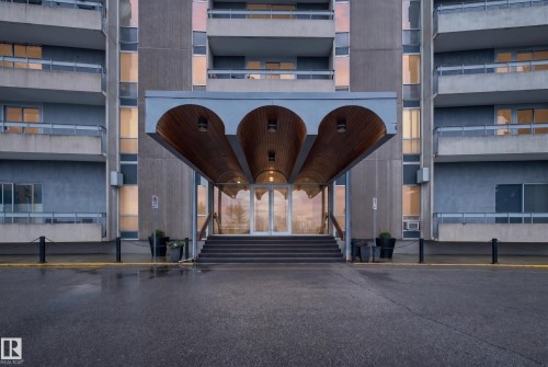 Multi-story building entrance with a covered portico featuring three arched wood-paneled ceilings and integrated lighting - #1804 10883 Saskatchewan Dr Nw, Edmonton, AB - Outdoor With Balcony