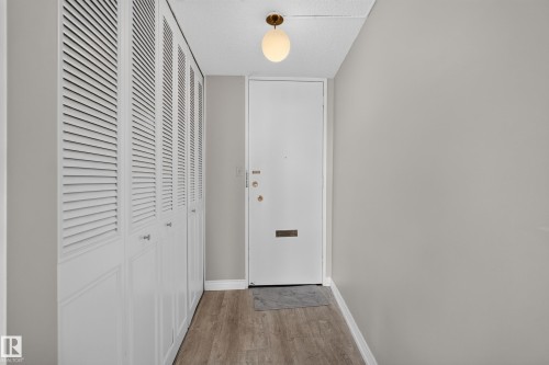 Entryway featuring wood-finish flooring, a white entry door with brass hardware, and a modern globe light fixture - #1804 10883 Saskatchewan Dr Nw, Edmonton, AB - Indoor Photo Showing Other Room