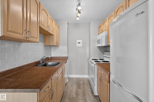 Galley kitchen featuring light wood-finish cabinetry, a subway tile backsplash, and a stainless steel sink with a chrome faucet - #1804 10883 Saskatchewan Dr Nw, Edmonton, AB - Indoor Photo Showing Kitchen