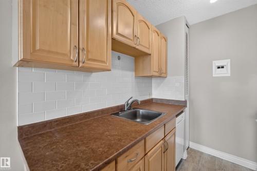 Kitchen featuring wood-finish cabinetry, stainless steel sink, white subway tile backsplash, and wood-finish flooring - #1804 10883 Saskatchewan Dr Nw, Edmonton, AB - Indoor Photo Showing Kitchen