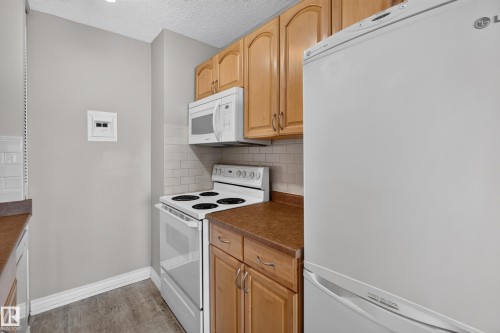 Compact kitchen featuring wood-finish cabinetry, white subway tile backsplash, and a wood-finish flooring - #1804 10883 Saskatchewan Dr Nw, Edmonton, AB - Indoor Photo Showing Kitchen