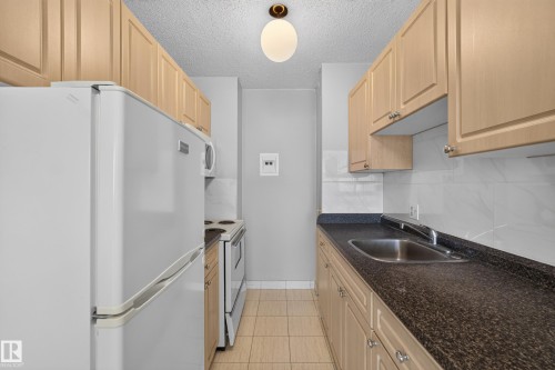 Galley kitchen featuring light wood-finish cabinetry, a white tile backsplash, and dark speckled countertops - #1508 10883 Saskatchewan Dr Nw Nw, Edmonton, AB - Indoor Photo Showing Kitchen