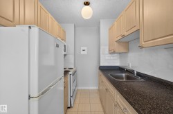 Galley kitchen featuring light wood-finish cabinetry, a white tile backsplash, and dark speckled countertops - 