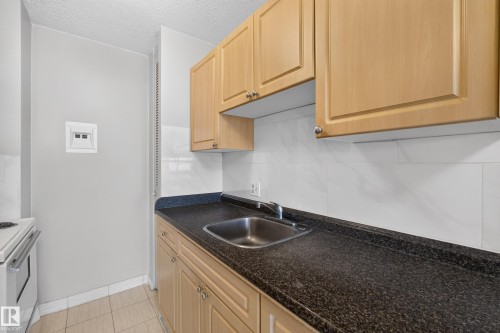 Kitchen featuring light wood cabinetry, dark speckled countertops, and a stainless steel sink - #1508 10883 Saskatchewan Dr Nw Nw, Edmonton, AB - Indoor Photo Showing Kitchen