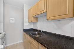 Kitchen featuring light wood cabinetry, dark speckled countertops, and a stainless steel sink - 