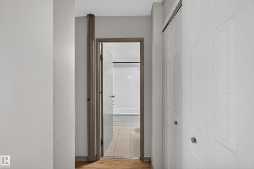 Hallway featuring wood-finish flooring, light gray wall paint, and a white six-panel bi-fold closet door with a silver knob - #1508 10883 Saskatchewan Dr Nw Nw, Edmonton, AB - Indoor Photo Showing Other Room