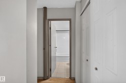 Hallway featuring wood-finish flooring, light gray wall paint, and a white six-panel bi-fold closet door with a silver knob - 
