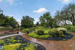 Expansive outdoor space featuring a brick patio, paved walkways, mature trees, and diverse plantings - 
