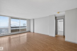Expansive living area featuring large windows, wood-finish flooring, light gray wall paint, a built-in baseboard heating unit, and an open doorway to an interior space with tile flooring - 