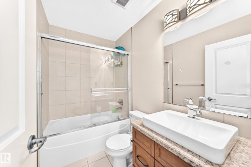Bathroom featuring a white bathtub with a sliding glass enclosure, a toilet, a wood-finish vanity with a vessel sink, and a speckled countertop - 2923 16 Street Nw, Edmonton, AB - Indoor Photo Showing Bathroom
