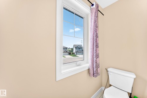 Vertical window with white trim, featuring a white toilet with visible plumbing, and light-colored walls - 2923 16 Street Nw, Edmonton, AB - Indoor Photo Showing Bathroom