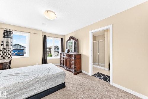 Carpeted room with neutral-toned walls, two windows, and an en suite bathroom featuring a glass-enclosed shower - 2923 16 Street Nw, Edmonton, AB - Indoor Photo Showing Bedroom