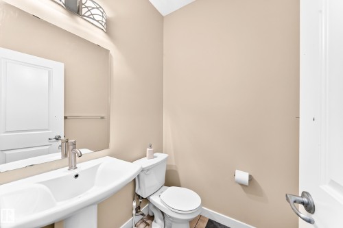 Bathroom featuring a pedestal sink, brushed nickel faucet, mirror, wall-mounted light fixture, and toilet - 2923 16 Street Nw, Edmonton, AB - Indoor Photo Showing Bathroom