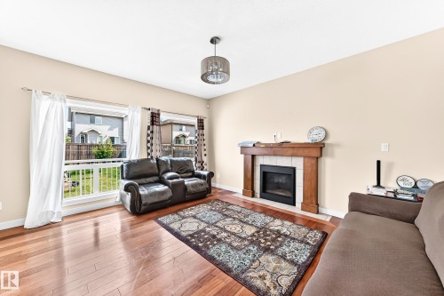 Living area featuring wood-finish flooring, a fireplace with a wood mantel and tile surround, and large windows overlooking the backyard - 2923 16 Street Nw, Edmonton, AB - Indoor Photo Showing Living Room With Fireplace