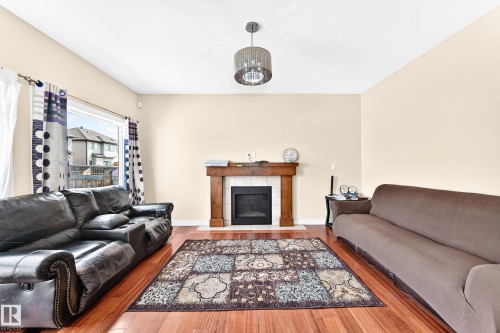 Spacious living area featuring a wood-finish floor, a large window, a fireplace with a wood mantle and tile surround, a vaulted ceiling, and a prominent ceiling fixture - 2923 16 Street Nw, Edmonton, AB - Indoor Photo Showing Living Room With Fireplace