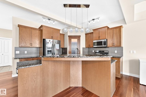 Spacious kitchen featuring a central island, wood-finish flooring, granite countertops, tile backsplash, and stainless steel appliances - 2923 16 Street Nw, Edmonton, AB - Indoor Photo Showing Kitchen