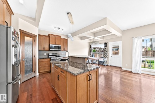 Kitchen featuring a granite-topped island, wood-finish flooring, stainless steel appliances, and wood cabinetry - 2923 16 Street Nw, Edmonton, AB - Indoor Photo Showing Kitchen