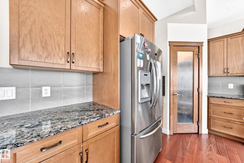 Kitchen featuring a stainless steel French door refrigerator, wood-finish cabinetry, speckled countertops, and a gray tile backsplash - 2923 16 Street Nw, Edmonton, AB - Indoor Photo Showing Kitchen